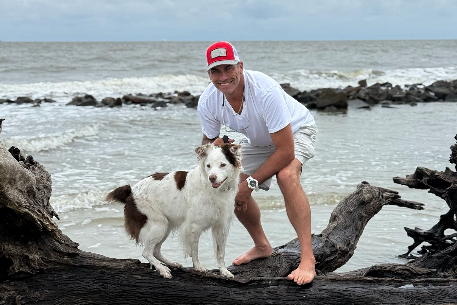 Barrett Sharpe with Lola on driftwood beside the water.